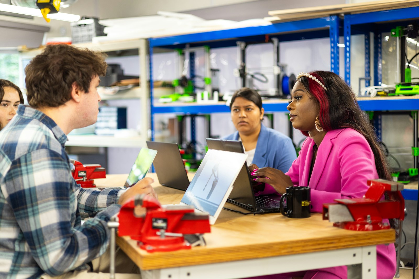Equipo diverso de ingeniería trabajando con portátiles en un laboratorio maker con impresoras 3D